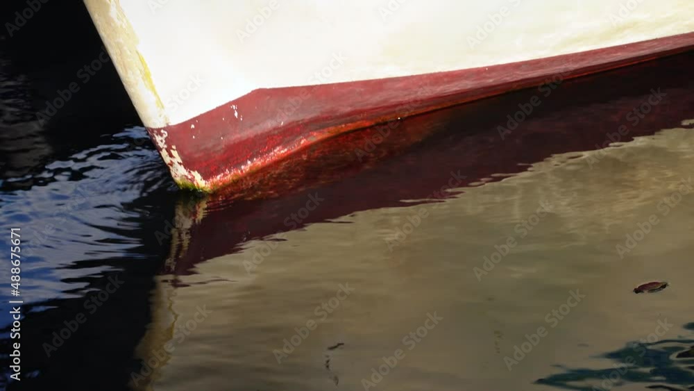 Bow of an old boat with peeling paint that floats on water on pier, swinging on waves, side view, close up. Smooth surface pond reflects surrounding world like a mirror Bow of an old boat with peeling paint that floats on water on pier, swinging on waves, side view, close up. Smooth surface pond reflects surrounding world like a mirror