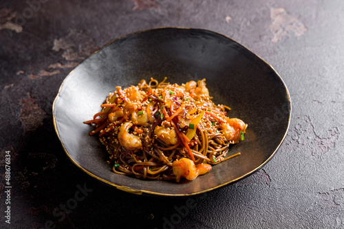 wok, soba noodles with shrimps and vegetables on dark stone table