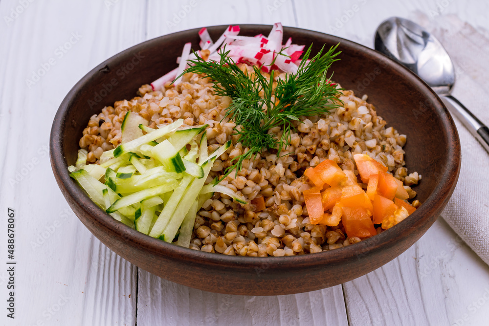 Boiled buckwheat in a plate with vegetables on white wooden table Boiled buckwheat in a plate with vegetables on white wooden table