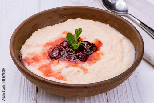 Photos semolina in milk with jam on white wooden table