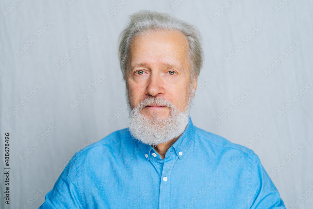 Close-up portrait of handsome gray-haired senior man unemotionally looking at camera on white isolated background. Front view of bearded mature aged gentleman posing in studio. Close-up portrait of handsome gray-haired senior man unemotionally looking at camera on white isolated background. Front view of bearded mature aged gentleman posing in studio.