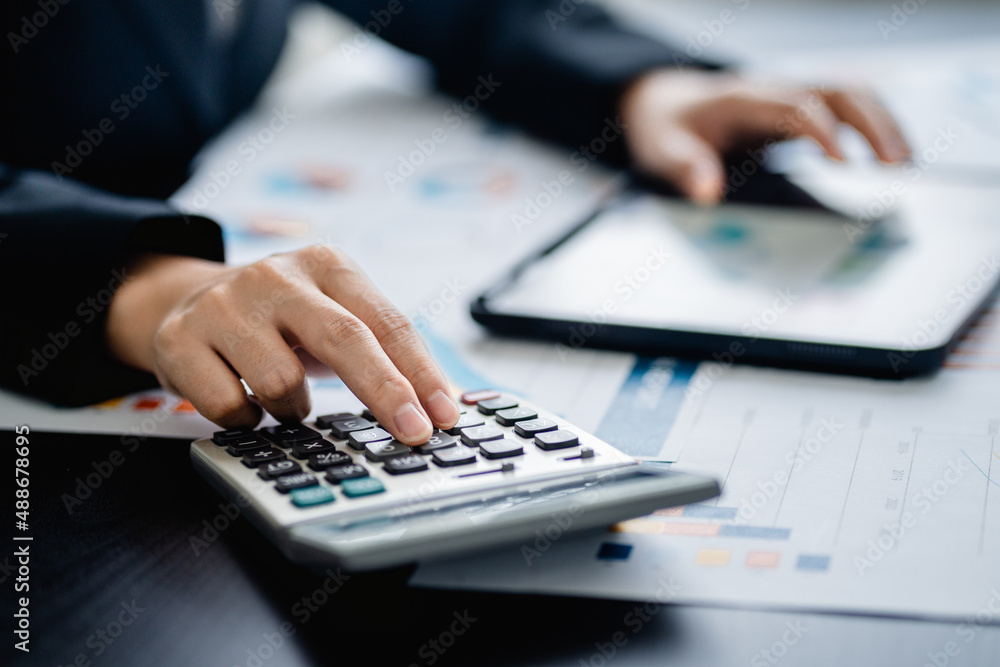 Close up of Businesswomen or Accountant using a calculator and laptop computer with analytic business report graph and finance chart at the workplace, financial and investment concept. Close up of Businesswomen or Accountant using a calculator and laptop computer with analytic business report graph and finance chart at the workplace, financial and investment concept.