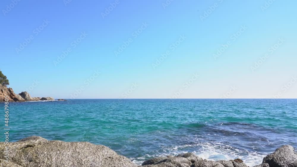 Sea waves crushes on rocks with clear blue sky at background