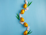 Creative Easter wave composition made from golden wooden eggs, pink marshmallow bunny and green grass on pastel blue background. Spring, easter concept. Flat lay, top view, copy space, square