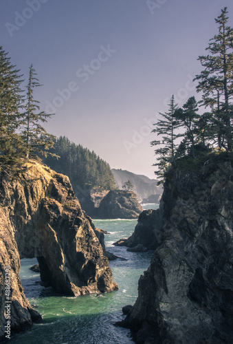 Sunset on natural bridges along the west coast of the Pacific Ocean, Oregon during the golden hour sunset - the sun's rays through the trees with dense vegetation. Beautiful seascape with rocks.
