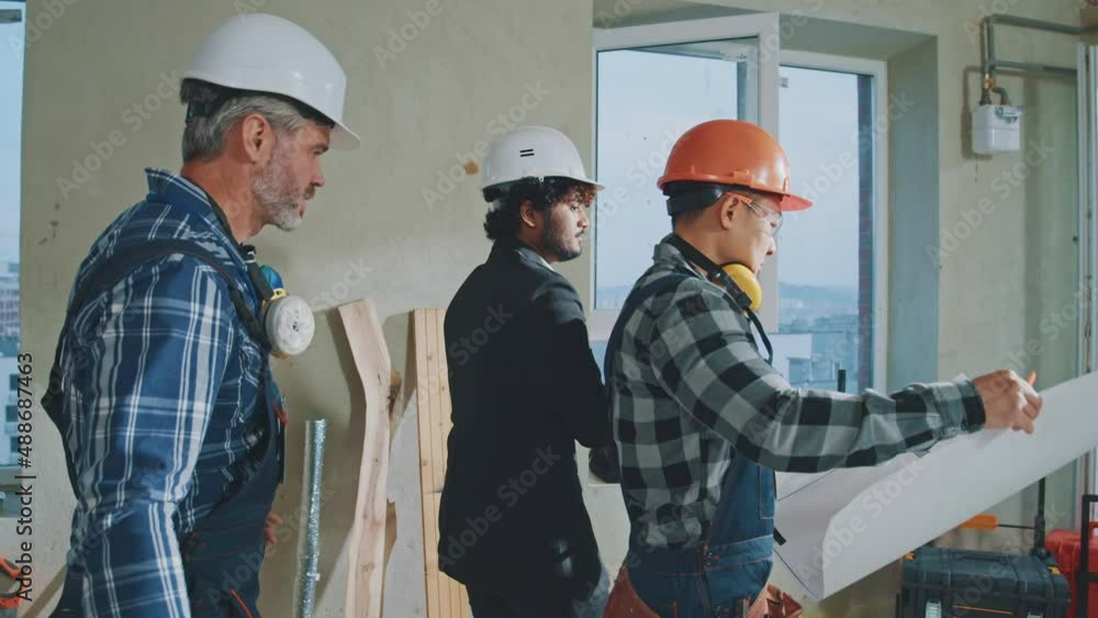 In building architect man in suit discussing with engineers or builders in hardhats checking plan details walking around. Talking, drawing on blueprint. Slow motion