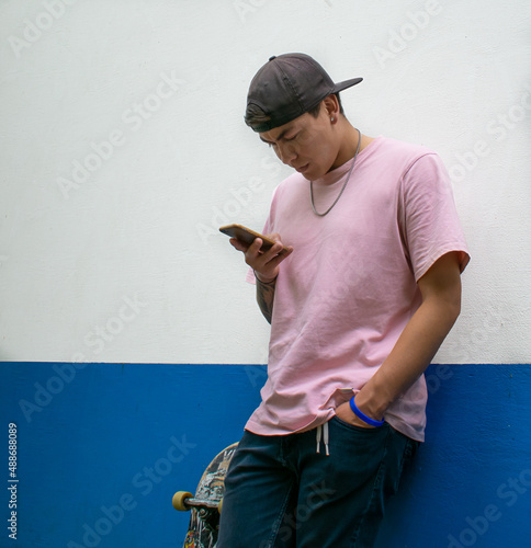 Young latin adult checking his smartphone. Cool serious skater in a white and blue background with copyspace.