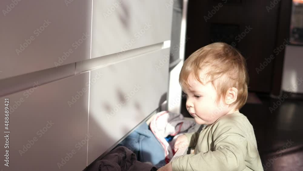 A cute child opens a chest of drawers with things and scatters. Mess in the house A cute child opens a chest of drawers with things and scatters. Mess in the house