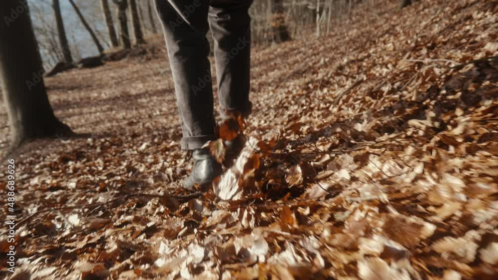 man in boots walking on forest floor with many leaves swirling around. sunny autumn day with water in the background. exploring nature in slow motion 4K. fall landscape. man in boots walking on forest floor with many leaves swirling around. sunny autumn day with water in the background. exploring nature in slow motion 4K. fall landscape.