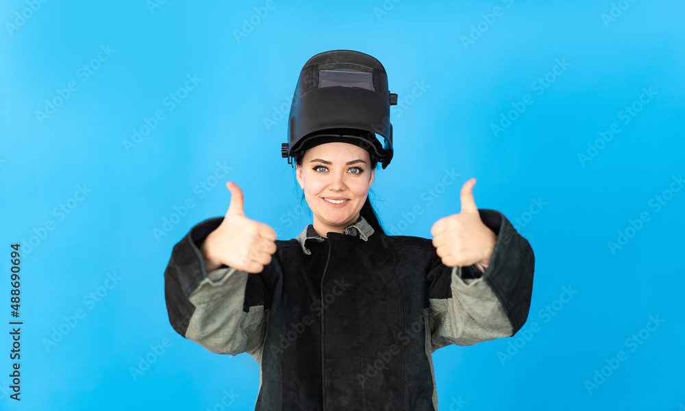 a welder girl in a protective mask looks into the camera and shows a thumbs up. a welder girl in a protective mask looks into the camera and shows a thumbs up.