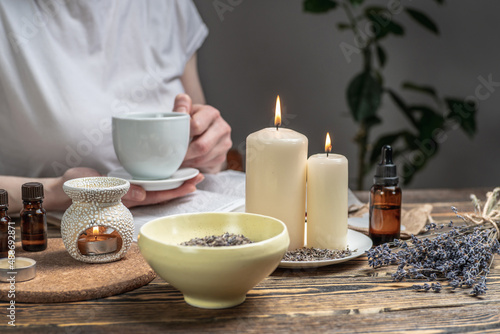 Woman is reading a book and drinking tea in atmosphere of harmony and relaxation. Aroma lamp with essential oils and burning candles on the wooden table