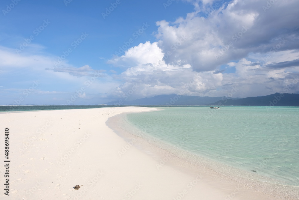 Pristine white sand remote, secluded tropical sandbar paradise island surrounded by turquoise ocean water and a single solo boat in the distance. 