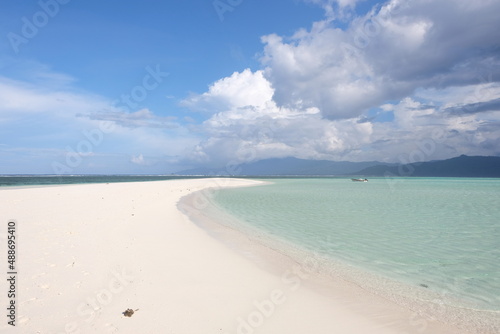 Pristine white sand remote, secluded tropical sandbar paradise island surrounded by turquoise ocean water and a single solo boat in the distance. 