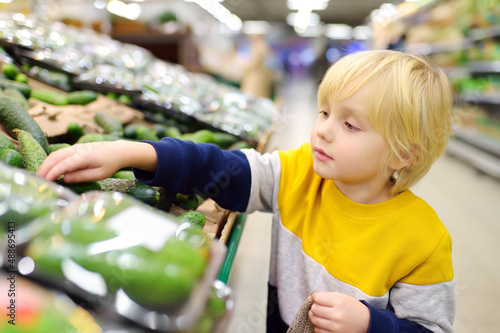 Cute little boy in a food store or a supermarket choosing fresh organic cucumbers. Healthy vegetables for kids. Shopping with child.