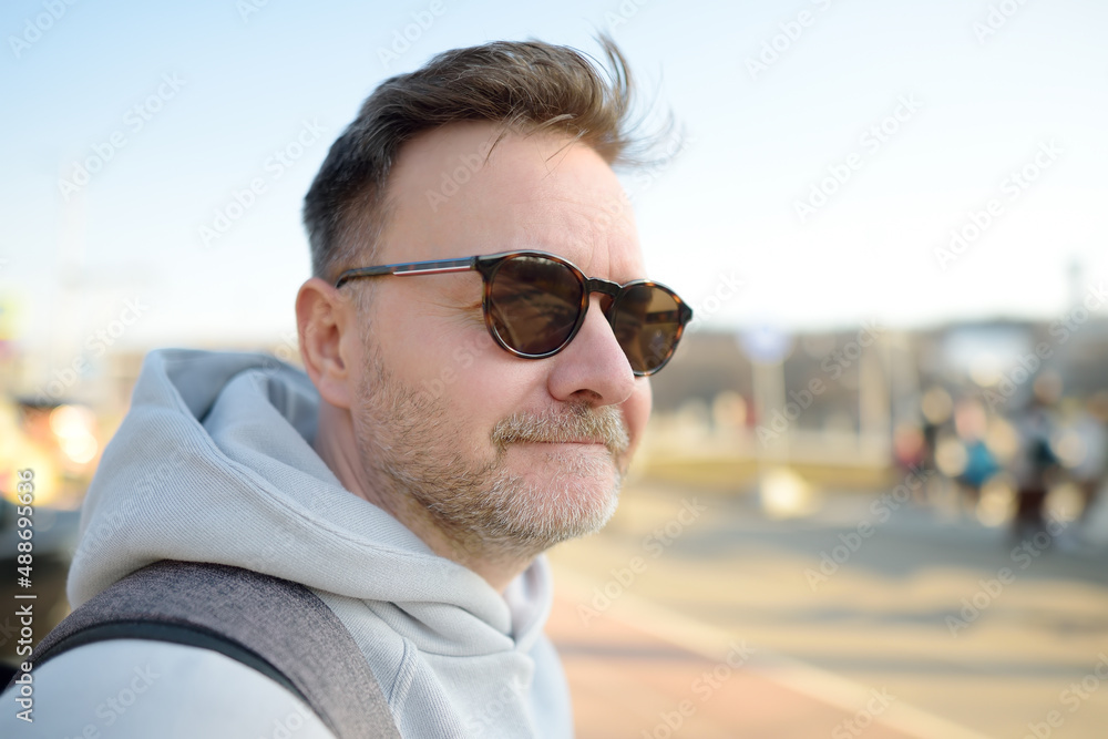 Handsome mature muscular man during a stroll in the city. Hipster in sunglasses walks on a sunny day. Active lifestyle of citizens. Urban entertainments. Handsome mature muscular man during a stroll in the city. Hipster in sunglasses walks on a sunny day. Active lifestyle of citizens. Urban entertainments.