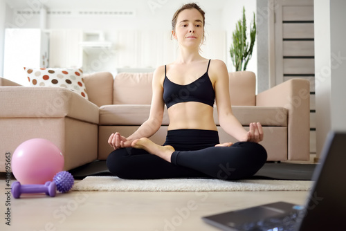 Distance sports fitness training. An attractive young woman does yoga or stretching online using a laptop at home. Meditation. Entertainment, learning and sports on the internet