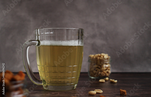 light beer in a glass mug with crackers and peanuts on a dark background