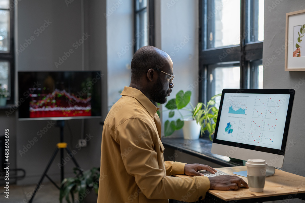 © pressmaster - Young modern economist in casual clothes working with financial data in front of computer while sitting by desk in office