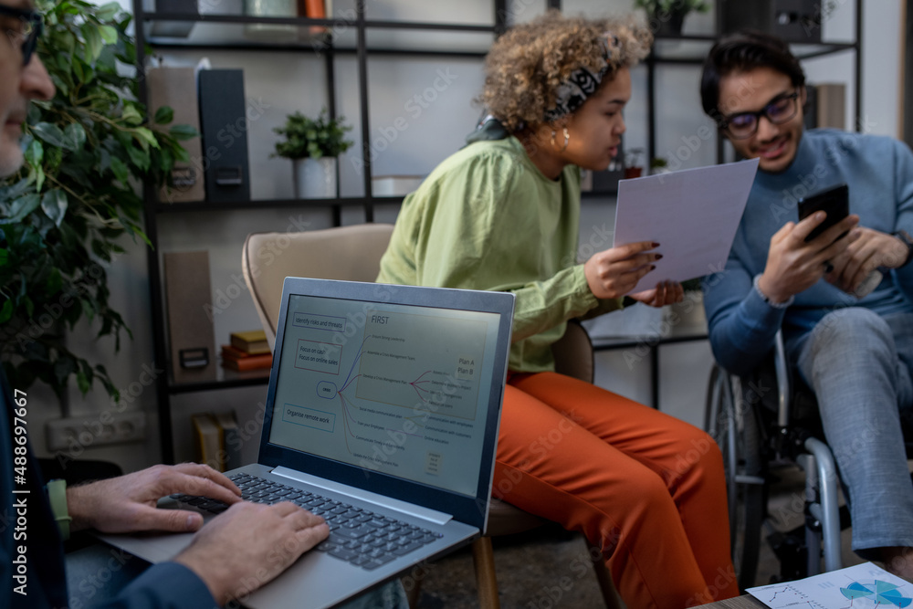 custom made wallpaper toronto digitalMature economist analyzing data on laptop screen against two young intercultural coworkers discussing financial document