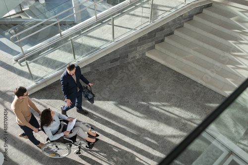 Above angle of confident ceo explaining business strategy to female colleague or partner with disability while moving along office center photo