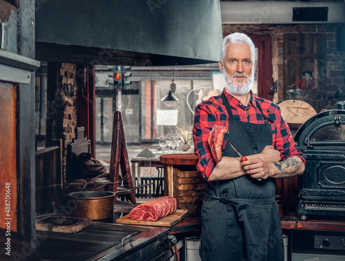 Elderly meat shop worker with apron and uncooked meat