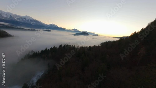 FPV Drone footage in Bled Slovenia captured at sunrise with in the nature with beautiful mountains and landscapes cover in fog and nice golden hour colors filmed in quick dynamic movement from above photo