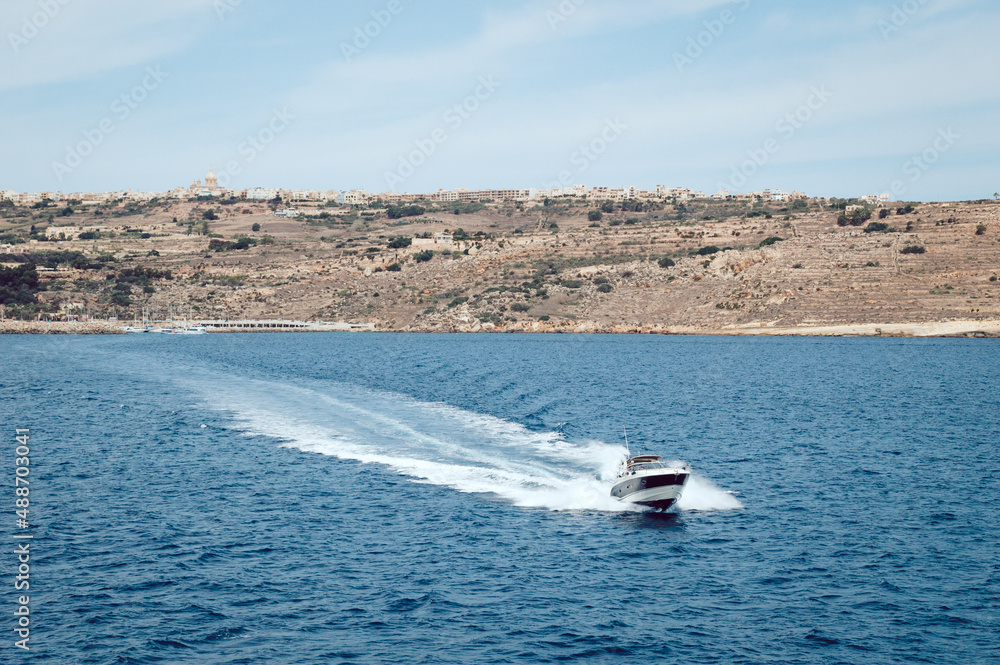 Fototapeta premium The boat sails from the island into the sea leaving waves on the water