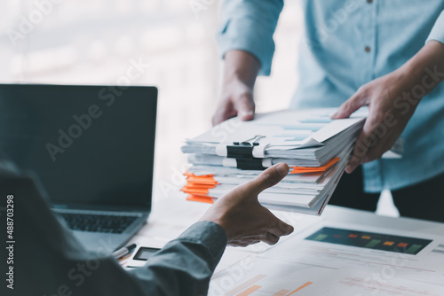 A young business man in a suit is managing paperwork in the office. Many paperwork that is not finished. Documents in the company about finance and information of the company.