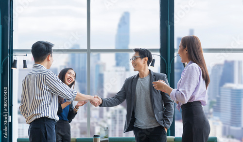 Asian business team leader congratulate his teammate employee for the outstanding achievement team performance by shaking hand in the modern office workplace with skyscraper view