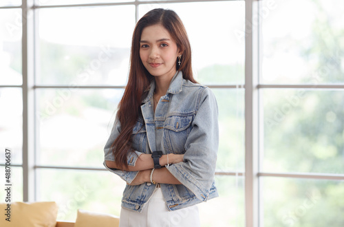 Portrait closeup shot of Asian young beautiful long brown hair female teenager fashion model in casual blue street denim jeans jacket standing smiling look at camera holding hand at chin crossed arm