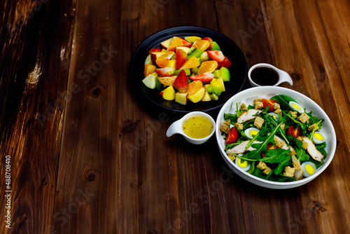 Top view shot of delicious healthy appetizers mixed sliced fresh raw fruits strawberry kiwi and green vegetables with boiled eggs salad dishes and dressing sauce placed on old vintage wooden table