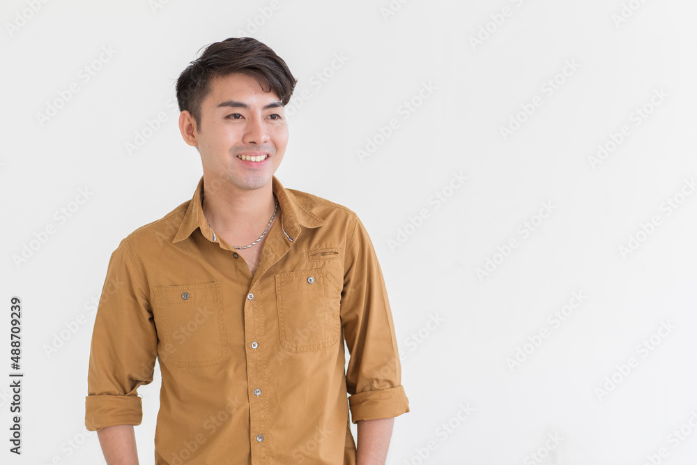 Portrait isolated cutout studio shot Asian young happy trendy male businessman model in casual brown long sleeve shirt with earring standing smiling holding hand in pants pocket on white background Portrait isolated cutout studio shot Asian young happy trendy male businessman model in casual brown long sleeve shirt with earring standing smiling holding hand in pants pocket on white background