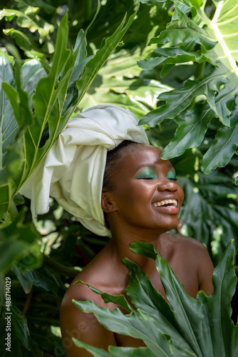 Portrait of a smiling young African woman, in leaves, wearing a  headwrap