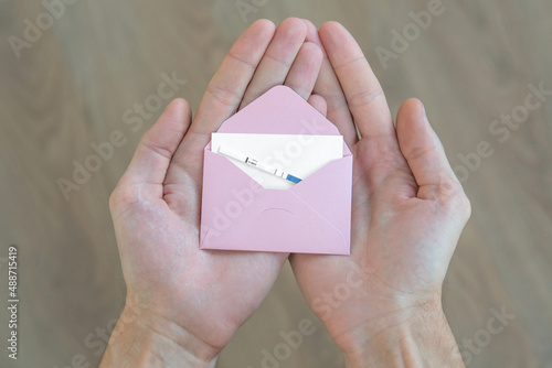 male hands hold a pink envelope with a white sheet of paper and a positive pregnancy test