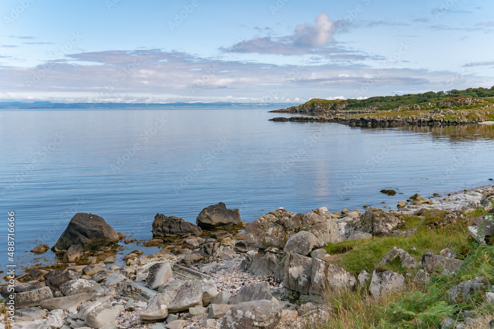 View of the coastline of the Isle of Islay with mainland Scotland on the horizon over clear calm blue sea water