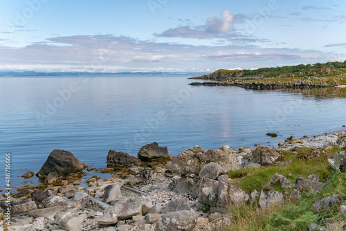 View of the coastline of the Isle of Islay with mainland Scotland on the horizon over clear calm blue sea water photo