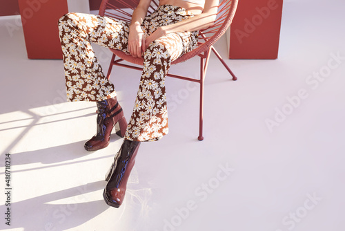 High fashion spring portrait of young elegant woman in retro outfit. Retro pants, panama hat, leather boots, flowers. 60s,