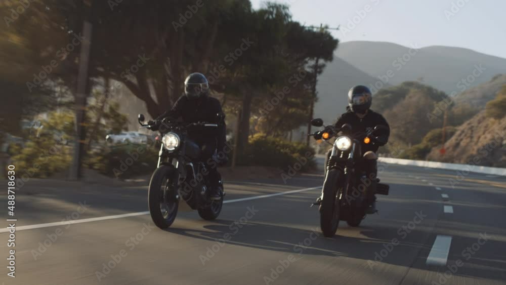 Summer ocean countryside trip concept. Men, wearing black helmets and tracksuits ride motorcycles. Biker outrides his friend at the picturesque coastal highway. High quality 4k footage Summer ocean countryside trip concept. Men, wearing black helmets and tracksuits ride motorcycles. Biker outrides his friend at the picturesque coastal highway. High quality 4k footage