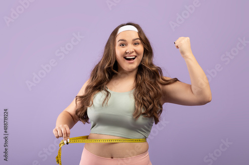 Photo Happy excited plus size european young lady in sportswear measure waist with mea