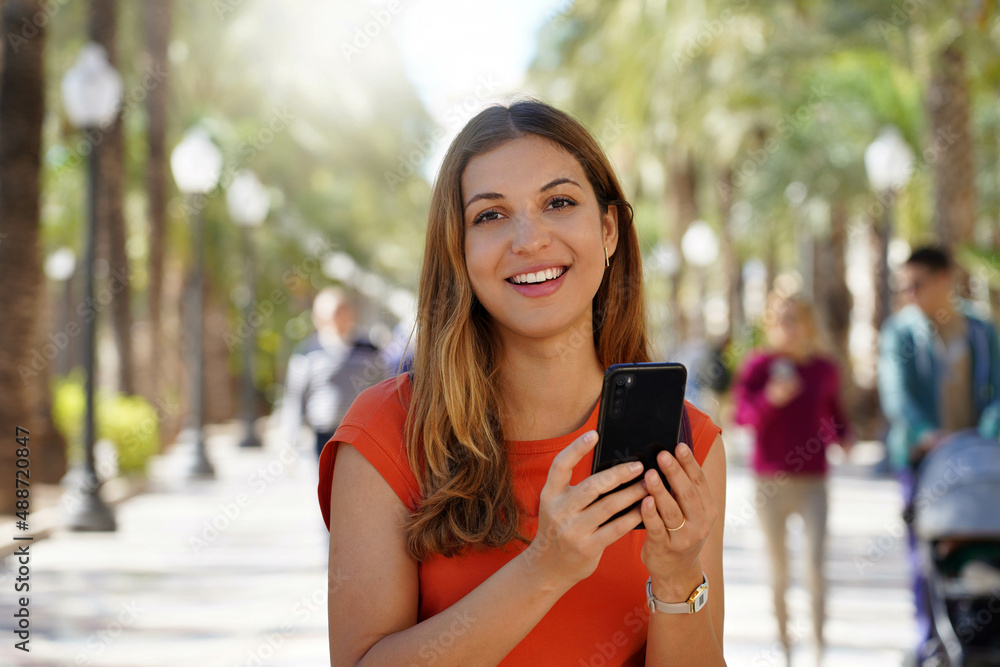 Young hispanic girl smiling happy using smartphone at the esplanade of Alicante, Spain