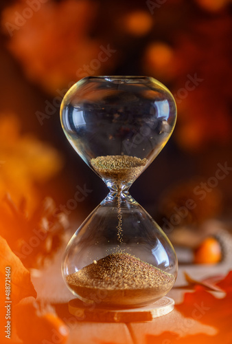 hourglass. red, orange leaves. concept of time, the onset of autumn season