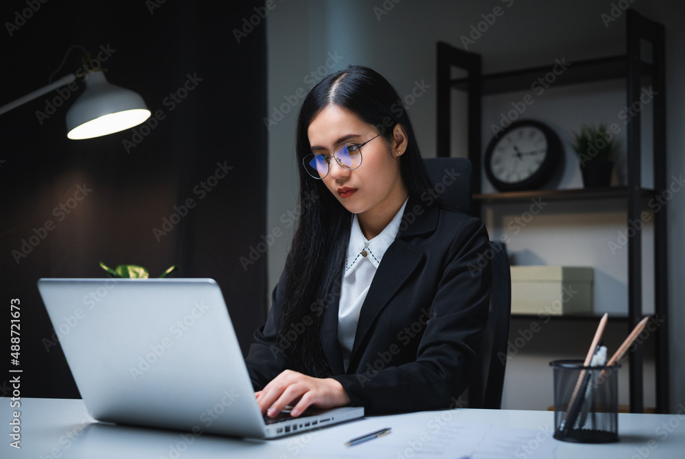 Young asian business woman working at late night. She was very busy checking paperwork and had to send the work before the deadline, feeling stressed. Sitting in the dark office at night. Young asian business woman working at late night. She was very busy checking paperwork and had to send the work before the deadline, feeling stressed. Sitting in the dark office at night.