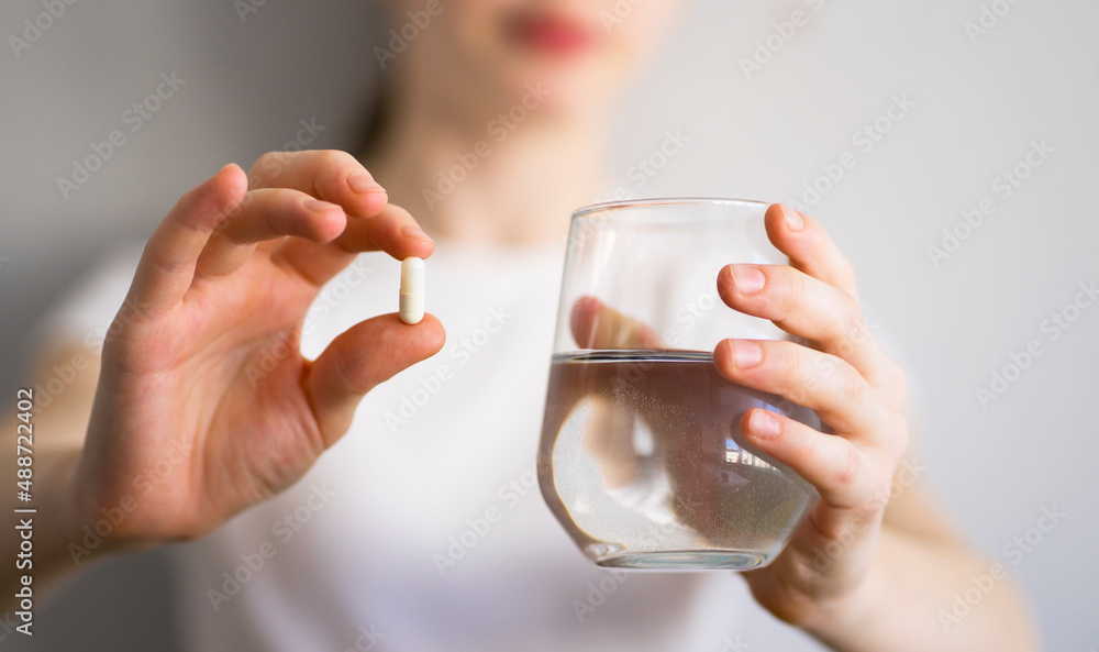 Girl holding a pill and a glass of water in her hands. Image with selective focus Girl holding a pill and a glass of water in her hands. Image with selective focus