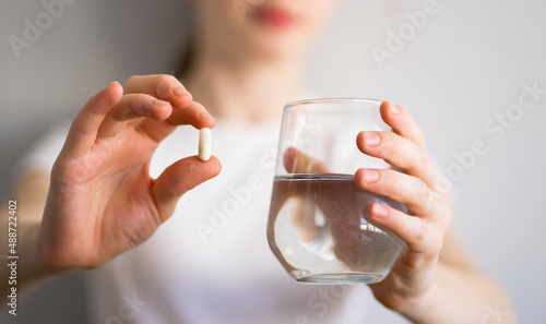 Girl holding a pill and a glass of water in her hands. Image with selective focus