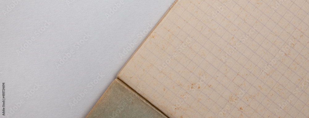 Fragment of a checkered notebook with yellowed old paper lying on a white sheet, close-up. Fragment of a checkered notebook with yellowed old paper lying on a white sheet, close-up.