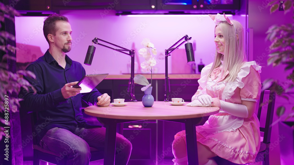 Man and pink maid cosplayer on video podcast in kitchen have a discussion Man and pink maid cosplayer on video podcast in kitchen have a discussion
