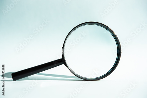 A black magnifying glass on a blue background, concept of search, research, looking for something.