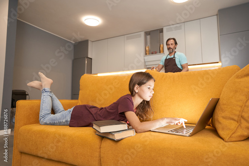 Girl lying on the sofa with a laptop near adult man
