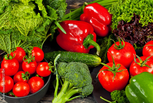 Cabbage, peppers, tomatoes, cucumbers, lettuce, cherry tomatoes, broccoli, arugula on a black background. variety of vegetables on a pile on a wooden table.