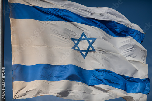 A large, blue and white flag of the State of Israel rippling in the wind on a sunny day during the national observance of the Independence and Memorial day holidays.